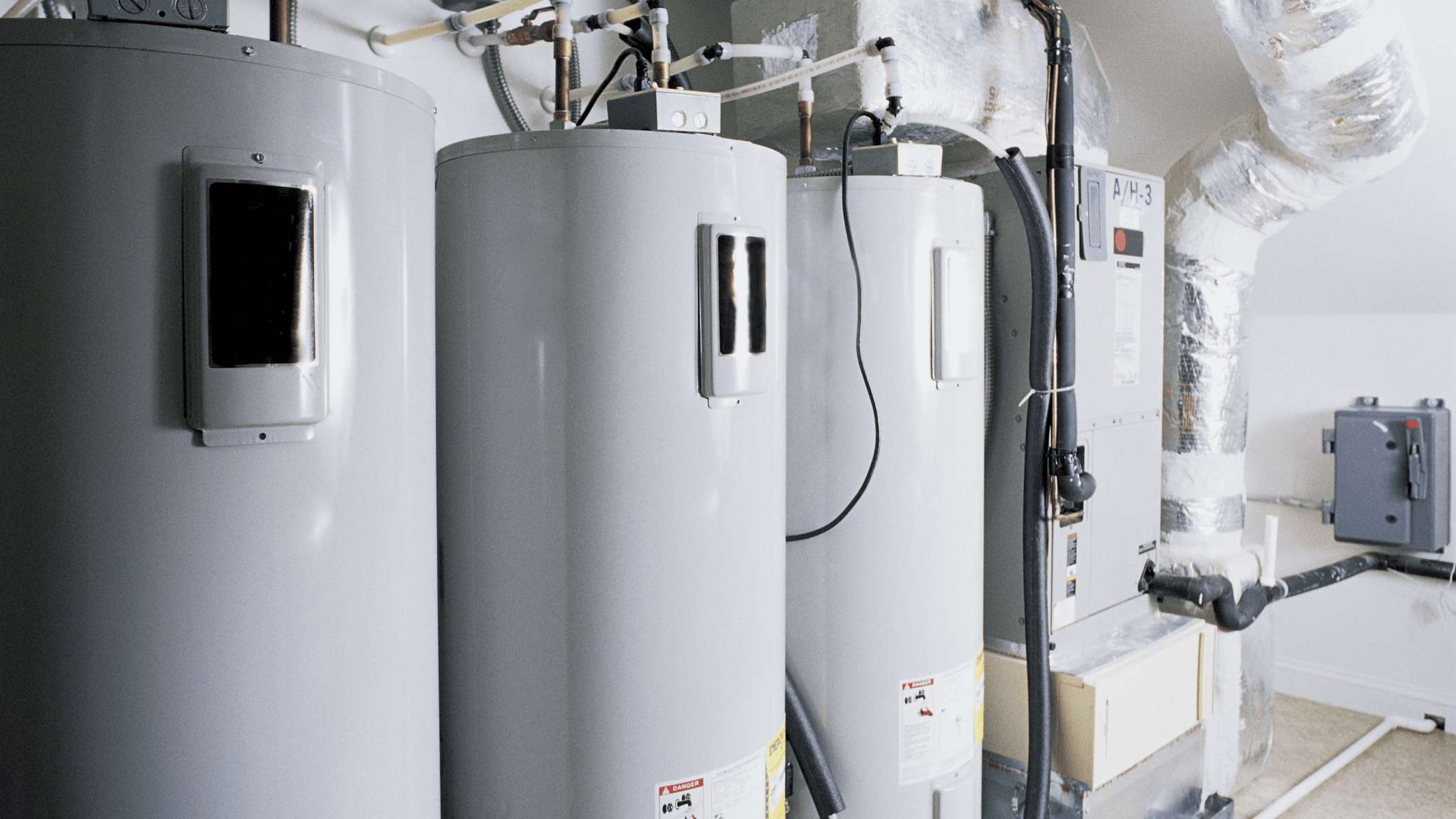 Row of residential water heaters and utility pipes needing fall maintenance